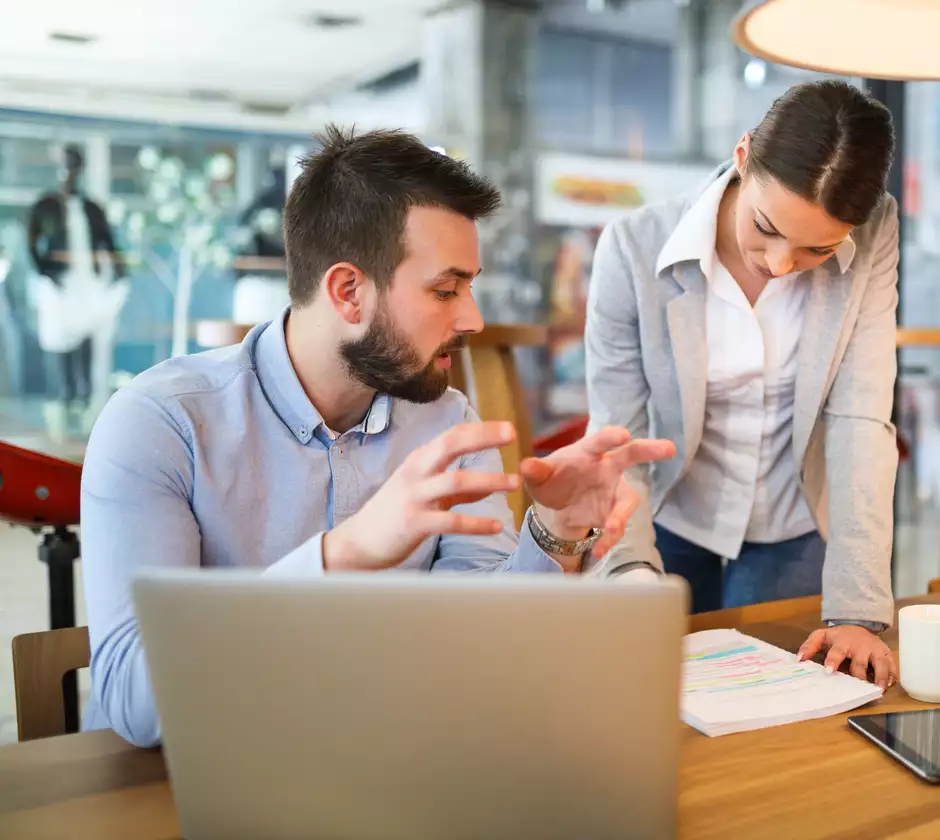 Une femme et un homme discute d'un projet à table avec un ordinateur et un bloc note