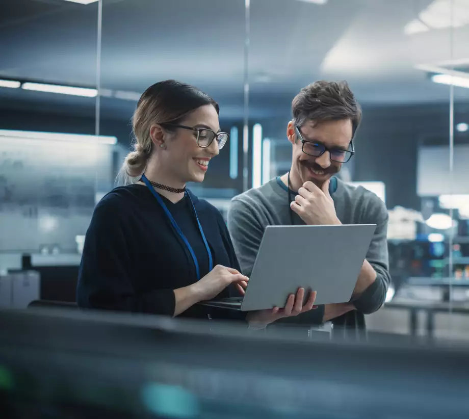 Un homme et une femme debout dans des bureaux qui regardent un ordinateur portable