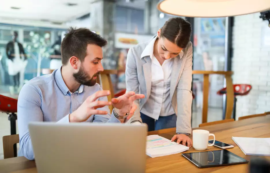 Une femme et un homme discute d'un projet à table avec un ordinateur et un bloc note